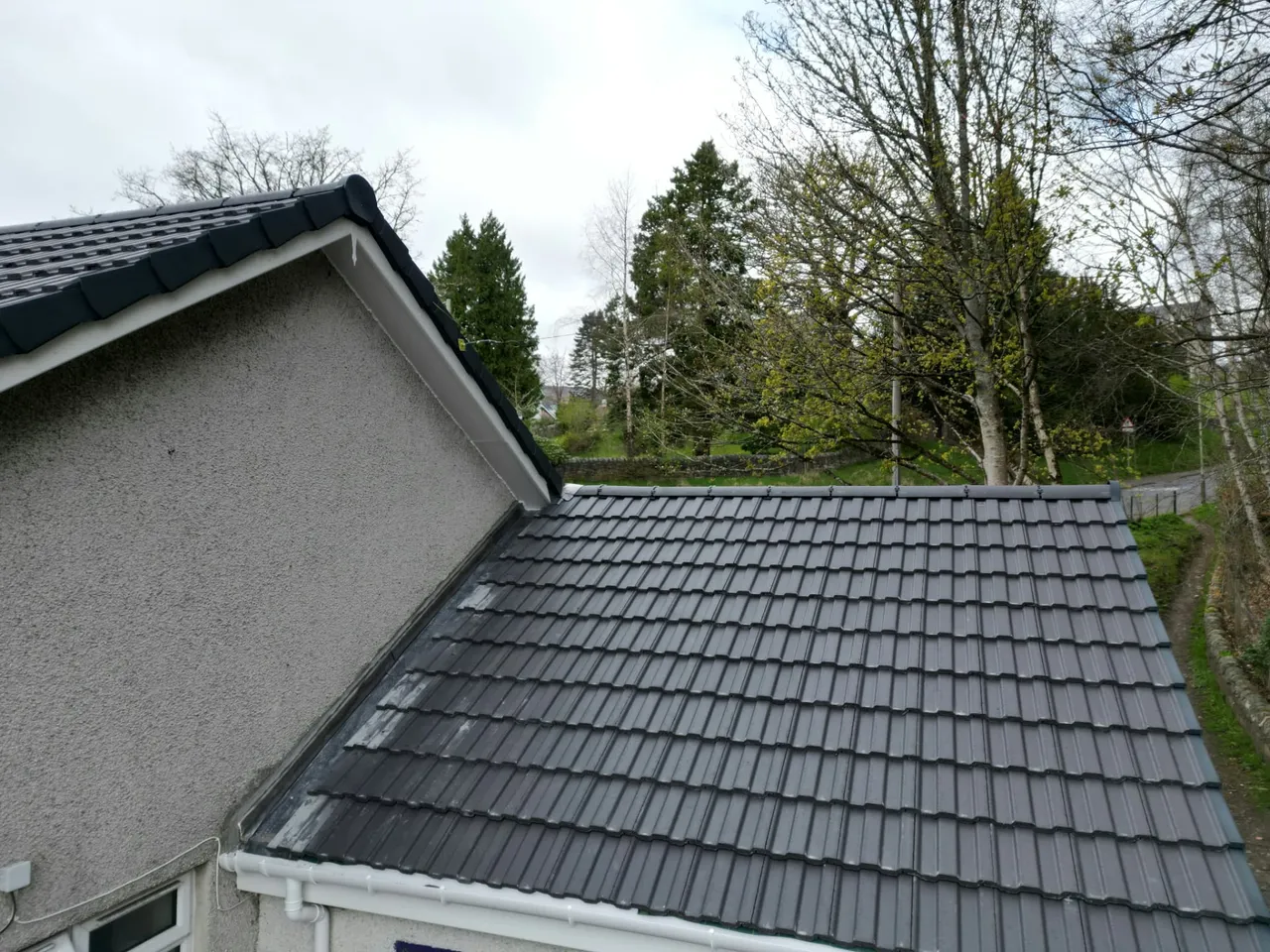 New interlocking roof tiles meeting a rendered gable wall with fresh fascias